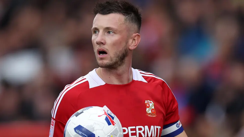 Ollie Clarke, kapten Swindon Town, menerima sanksi larangan tampil selama tujuh pertandingan menyusul tindakan berbahayanya.